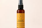 A 100ml amber glass spray bottle of 'The Beauty Brand' Moisturising Mango Seed Retinolmo Spray, featuring a mustard yellow label and black spray nozzle, set against a solid cream background.