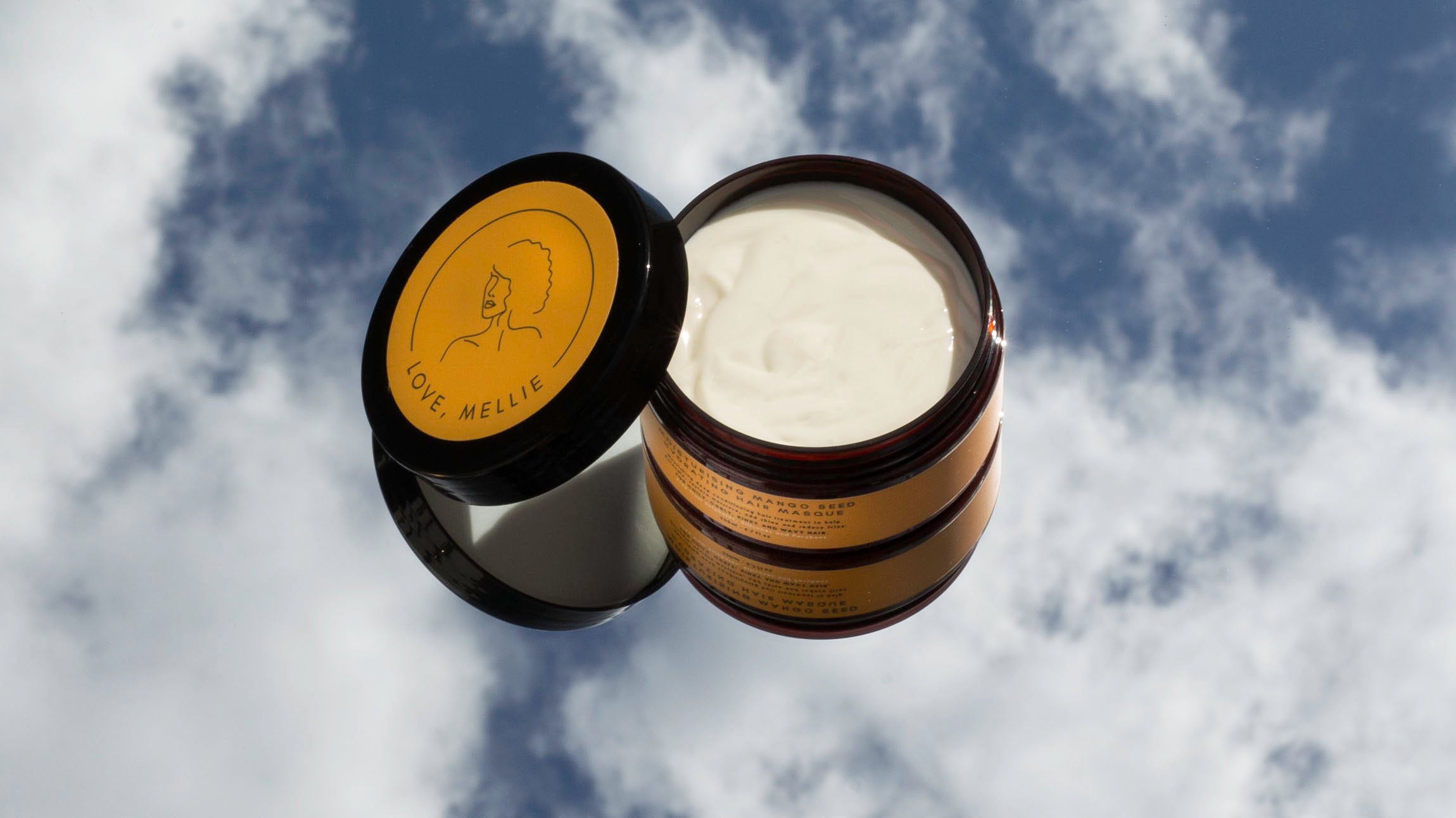 Open jar of thick hair mask with a cloudy sky background